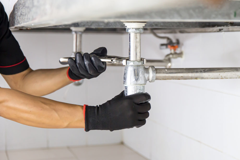 plumber using a wrench to repair a water pipe under the sink Gilbert, AZ